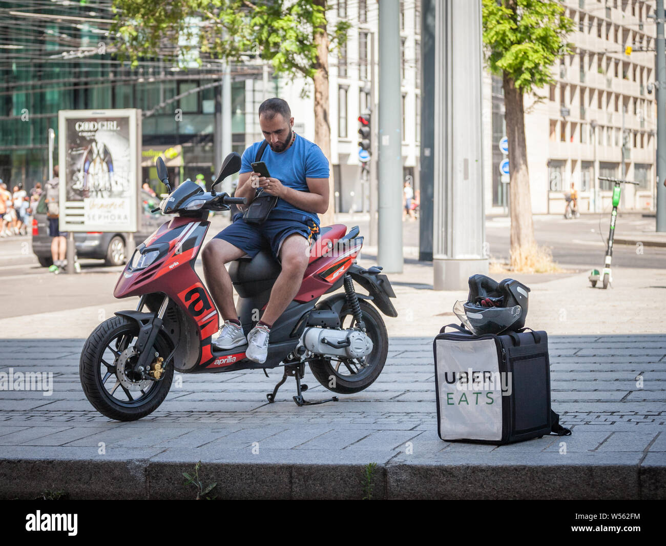 LYON, FRANCE - 13 juillet 2019 : Uber mange logo sur le sac d'un livreur sur son scooter, en utilisant son smartphone à attendre la prochaine commande de nourriture d'un Banque D'Images