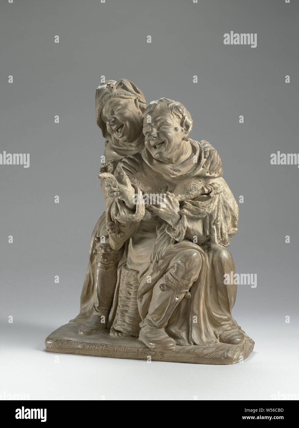 Rire deux bouffons, l'un assis sur un panier renversé trois-quarts vers la droite et avec la tête vers la gauche, l'autre, avec la tête dans la même direction, se dresse avec ses genoux repliés derrière lui avec ses mains sur ses épaules, l'air vont dans le même sens. Ils ont bombé, visages de sourire avec la bouche ouverte, dans laquelle la langue et les dents sont visibles. Les points jester assis à la main droite de l'avant et tient un bâton de bulles (karwats avec bulles ?) en face de la poitrine avec l'autre. Il y a une verrue sur la joue. Il porte un capuchon avec un ourlet décoré à l'encolure Banque D'Images