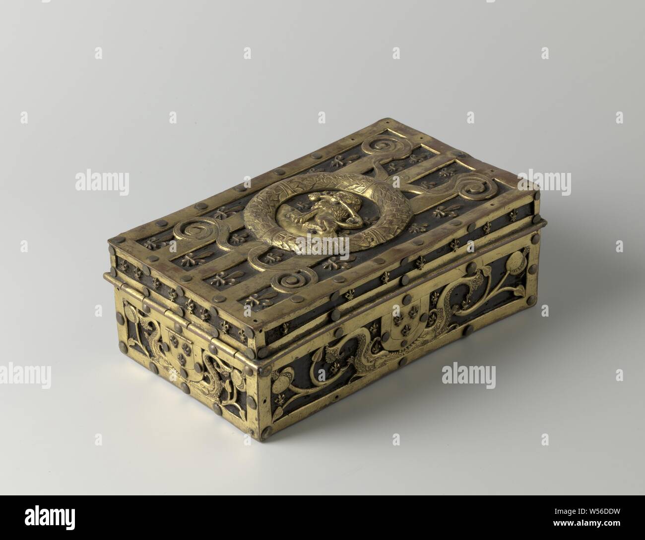Boîte en bois avec châssis en cuivre, de forme allongée boîte en bois carré, montés avec des bandes de cuivre doré, entre lesquels sont des feuilles. En haut entre les bandes de nénuphars, au milieu une lourde couronne de laurier, à l'intérieur de laquelle elle sur un lion assis avec une grenade dans la bouche. Sur le grenat soie branches et dauphins, entre lesquels les armes de France (trois fleurs). Sur la face avant l'arme comme une contre-plaque. Il est ouvert quand le clou est glissé., anonyme, 1500 - 1525, le bois (matière végétale), le cuivre (métal), dorure, h 11,5 cm × 31,0 cm × w 18,5 cm Banque D'Images
