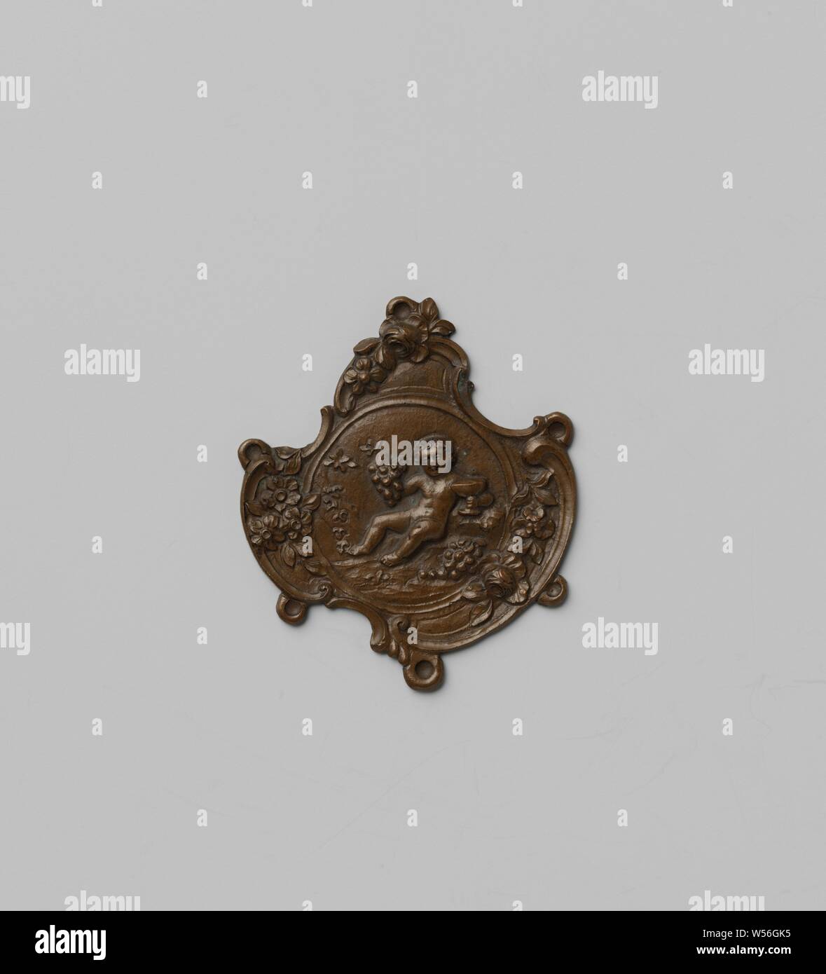 Modèle pour un élément décoratif d'une châtelaine, la plaque d'un modèle de moule a un médaillon entouré de fleurs et d'ornement rococo avec un putto avec grappe de raisins et calice. Le long des bords six yeux pour fixer les liens., anonyme, Amsterdam, c. 1750 - c. 1775, le cuivre (métal), h 4,1 cm × l 3,6 cm Banque D'Images