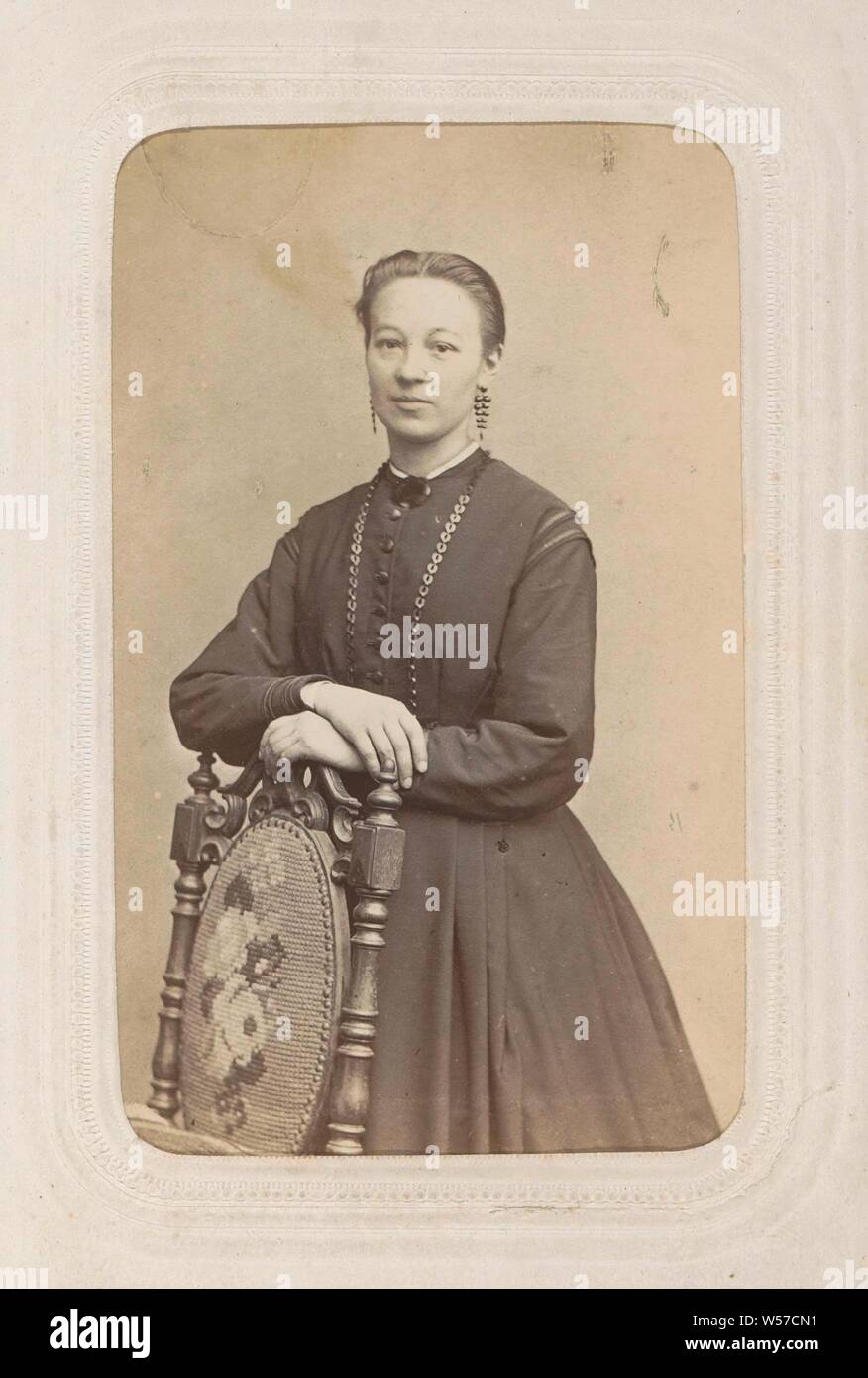 Portrait d'une femme dans une robe longue, debout contre un dossier de chaise, une partie de l'album photo avec 26 cartes de visite des membres du clergé catholique., robe, robe de chambre, studio, photographe, Maastricht, Pierre Weynen & Fils, c. 1860 - c. 1870, carton, papier, papier photographique, à l'albumine, h 90 mm × w 58 mm Banque D'Images