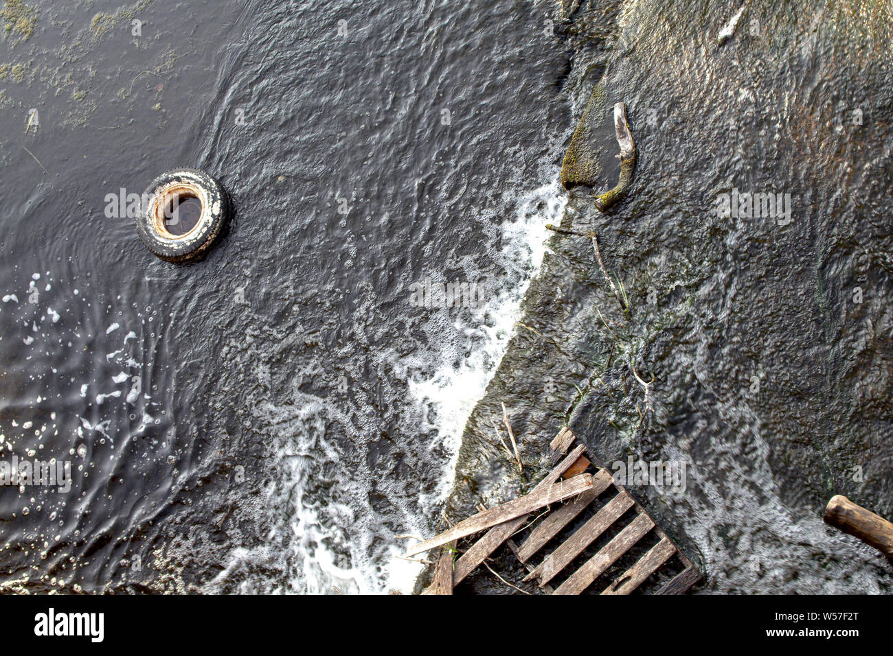 Un pneu et une palette en bois ont été éliminées sur une surface rocheuse dans les eaux du bord d'une rivière, et sont vues de dessus. Banque D'Images