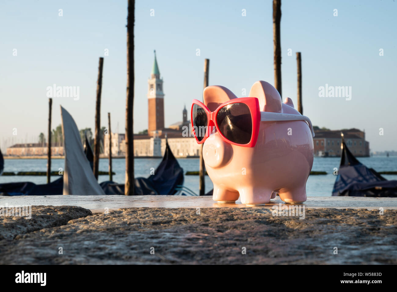 Close-up of Pink Piggy Bank Wearing Goggle gardé en face de San Giorgio Maggiore Banque D'Images