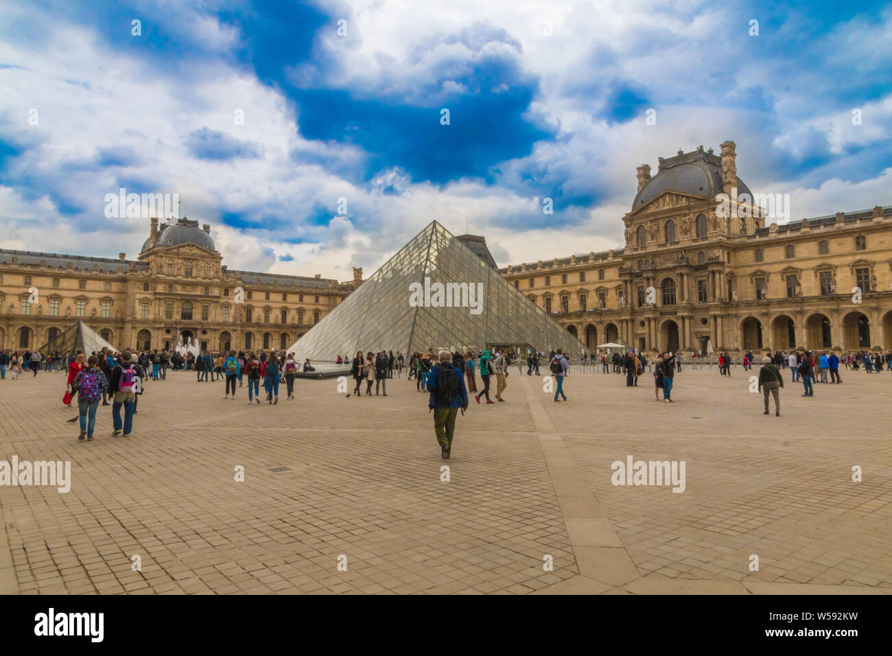 Vue panoramique sur le célèbre musée du Louvre à Paris. Dans la cour un mâle visiteur est en marche vers l'emblématique pyramide de verre du Louvre, l'un des... Banque D'Images