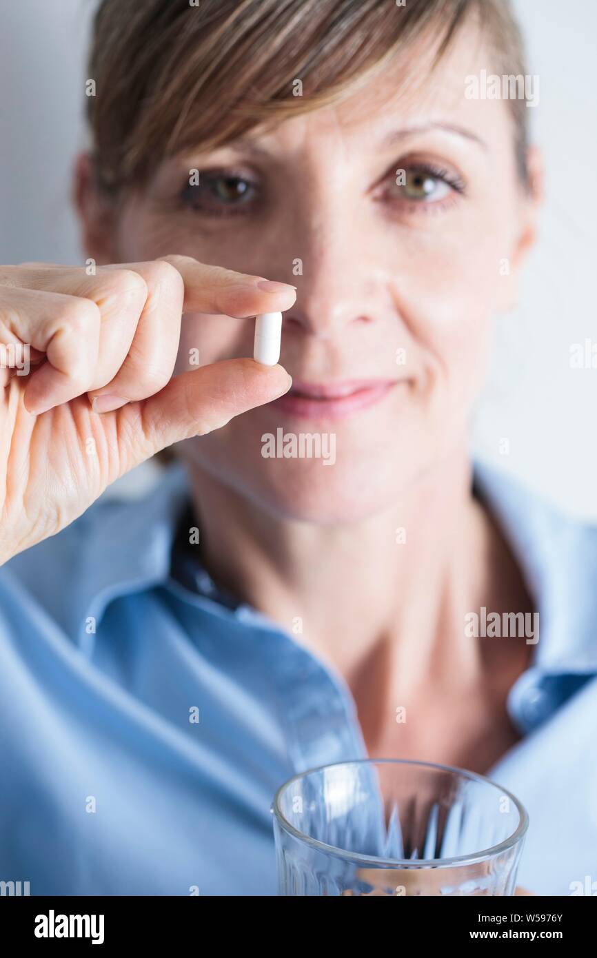 Femme tenant un comprimé d'ibuprofène entre ses doigts. Banque D'Images