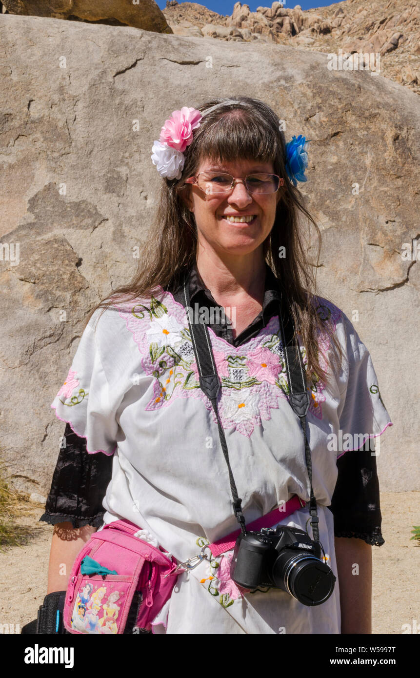 Les femmes avec de longs cheveux bruns et des fleurs dans ses cheveux contre un fond rocheux. La femme a un appareil photo Nikon autour du cou. Banque D'Images