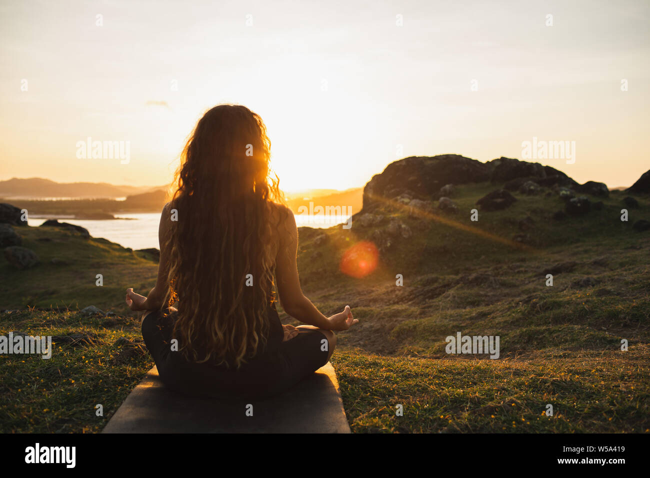 Woman meditating yoga seul au lever du soleil sur les montagnes. Vue de derrière. Style de voyage relaxation spirituelle concept. Harmonie avec la nature. Banque D'Images