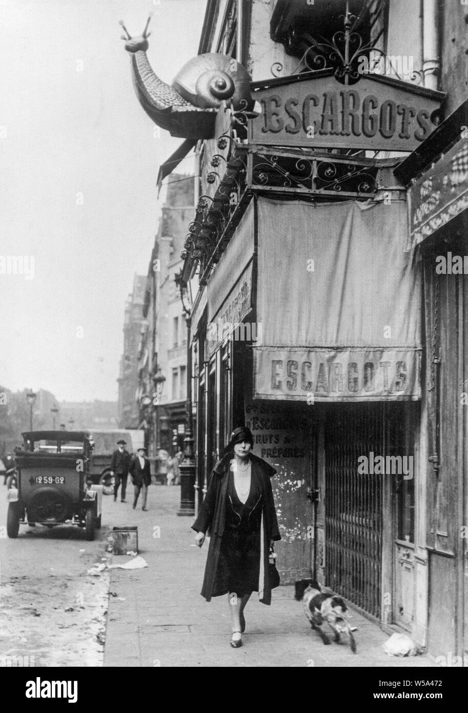 Au début du xxe siècle une photographie en noir et blanc prises à Paris, France. Photo montre une femme en passant devant un restaurant escargot, Escargots ou restaurant. Un grand modèle d'un escargot se trouve au-dessus du restaurant. Banque D'Images