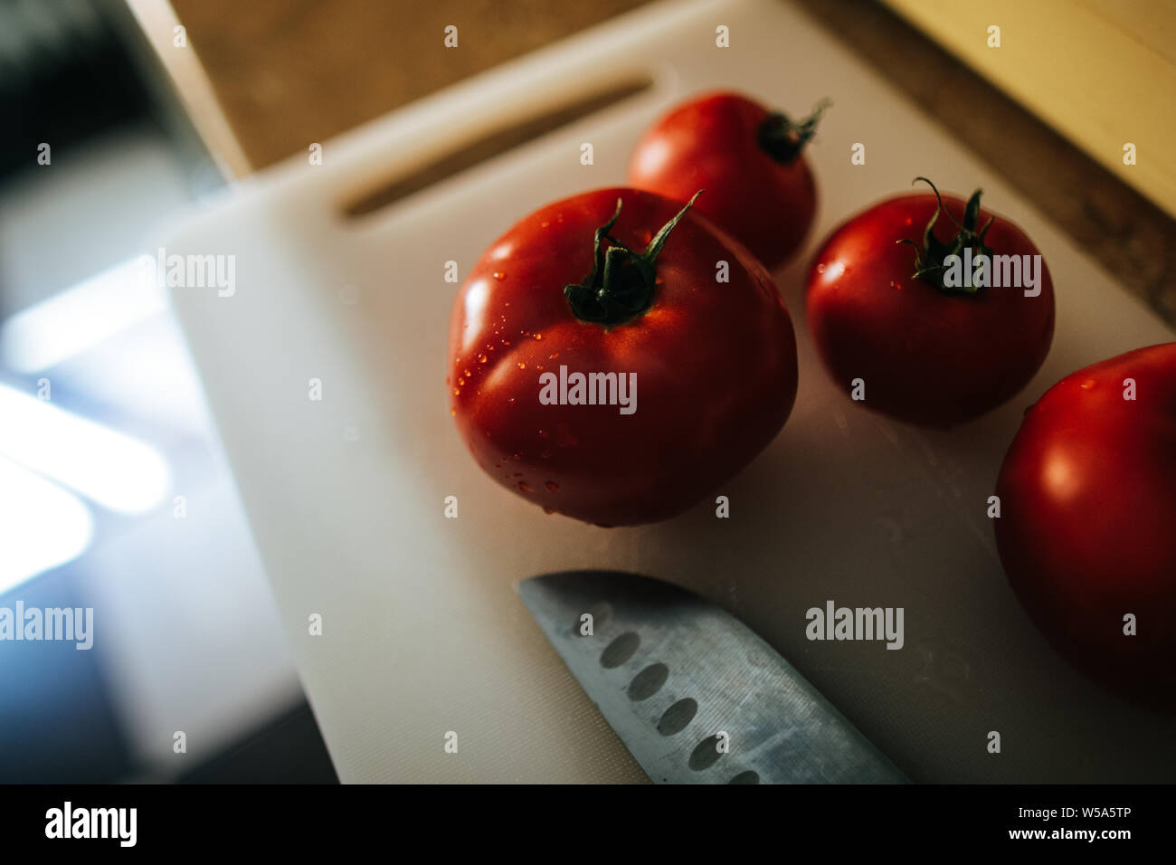 Les tomates fraîchement cueillies du jardin dans la cuisine sur une planche à découper en plastique et à proximité d'un couteau chef Banque D'Images