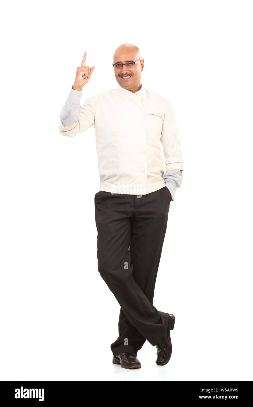 Smiling Chef avec ses mains dans les poches et pointant vers le haut Banque D'Images Smiling Chef avec ses mains dans les poches et pointant vers le haut Banque D'Images