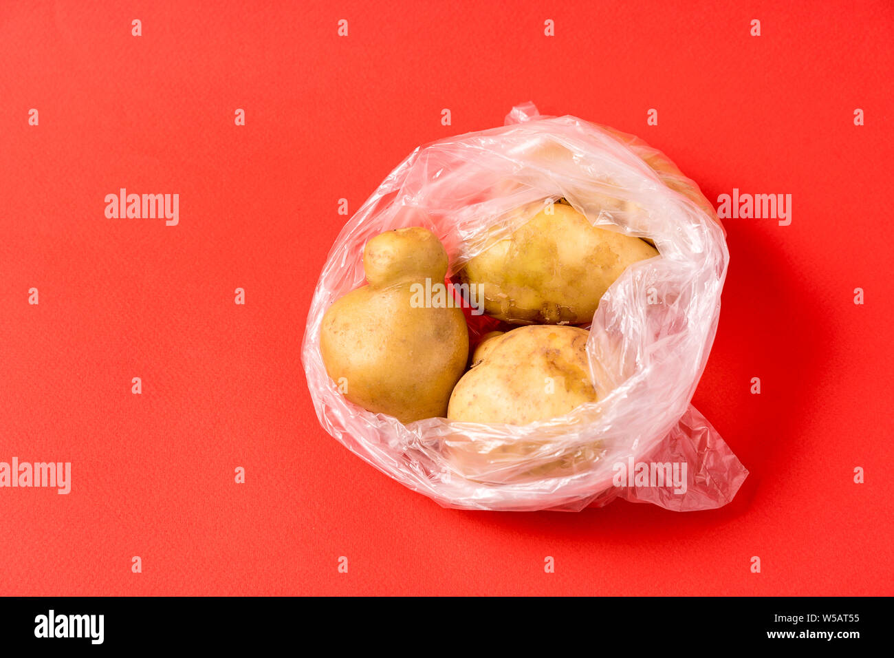 Vue avant les pommes de terre dans un sac plastique sur fond rouge. Image montre le harmness à l'aide de sacs de stockage de l'alimentation artificielle. Banque D'Images
