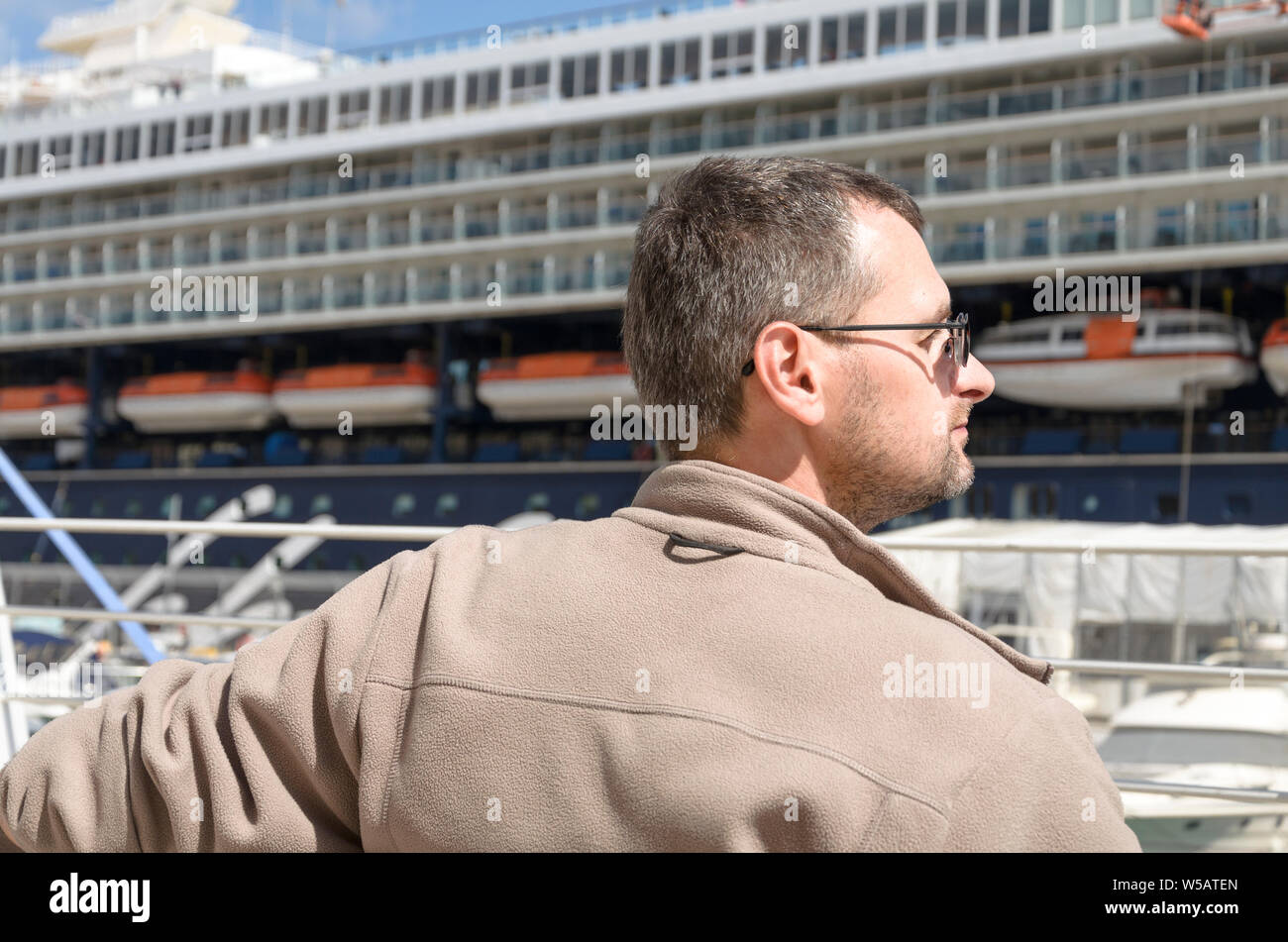 Un homme d'âge moyen dans les verres l'observation d'un grand bateau de croisière dans un port Banque D'Images