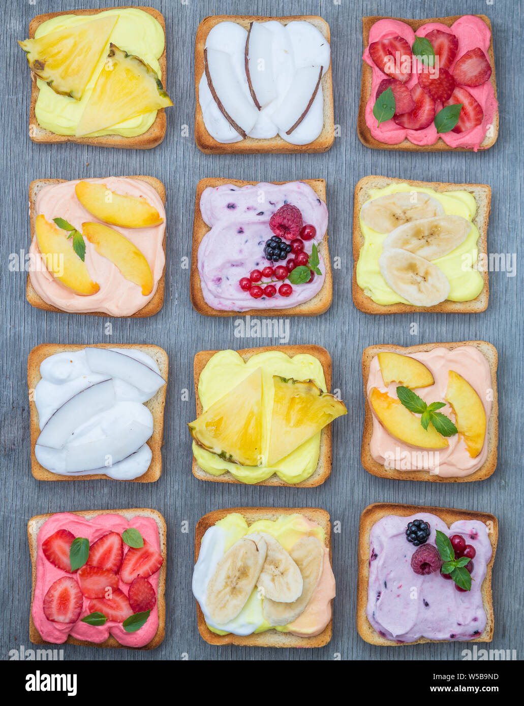 Un assortiment de toasts avec fruits et de baies sur wipped crème sur une planche de bois sur un fond clair. Dessert maison traditionnelle d'été. Banque D'Images