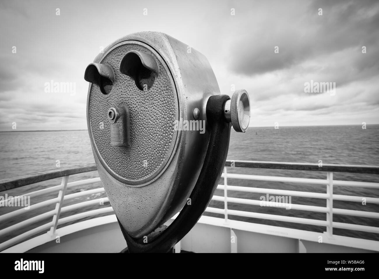 Gros plan en noir et blanc d'un télescope d'observation vintage à pièces de monnaie sur une terrasse d'observation surplombant l'océan Banque D'Images