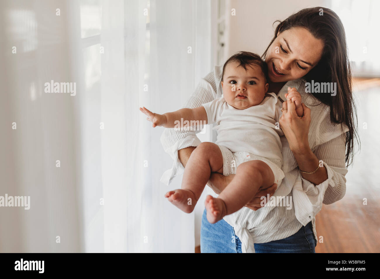 Young mother holding baby daughter and smiling in studio lumière naturelle Banque D'Images