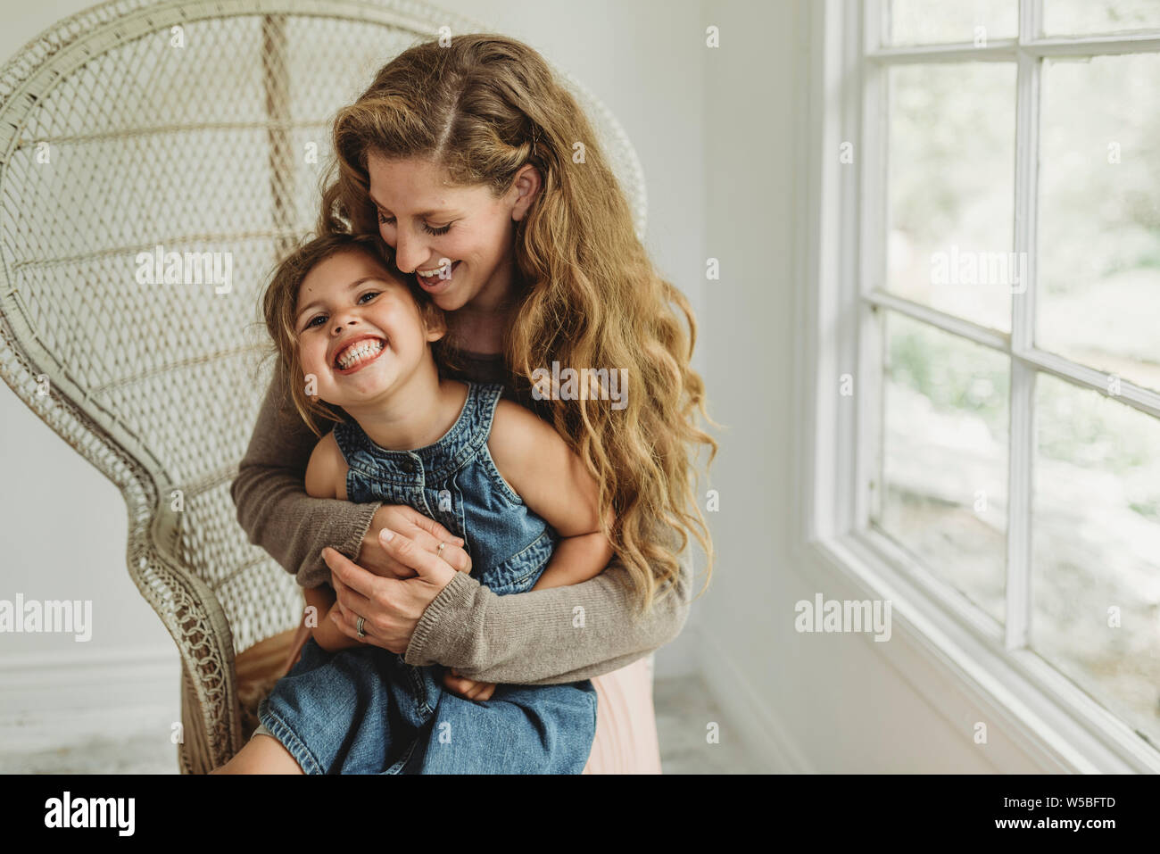 Fille étant détenu par mère en fauteuil et boho smiling in studio Banque D'Images