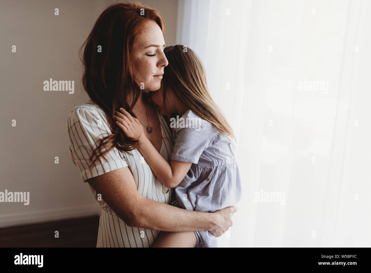 Jeune mère de câlins avec jeune fille en fermant les yeux en studio Banque D'Images