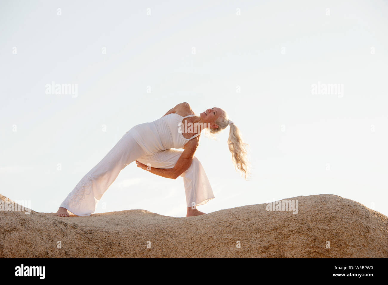 Senior woman in yoga pose sur les rochers. Banque D'Images
