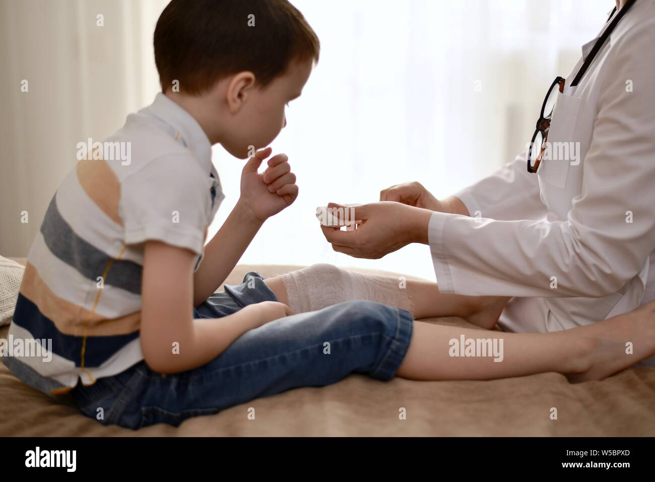 Les mains du médecin bandage soigneusement le genou blessé à l'enfant une surveillance étroite. Banque D'Images