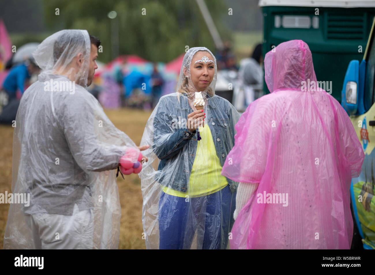 Standon, UK. Samedi 27 juillet 2019 les amateurs de festivals. eating ice cream portant la pluie ponchos à Standon Composant situé dans le pittoresque en raison de Standon Seigneurie © Jason Richardson / Alamy Live News Banque D'Images