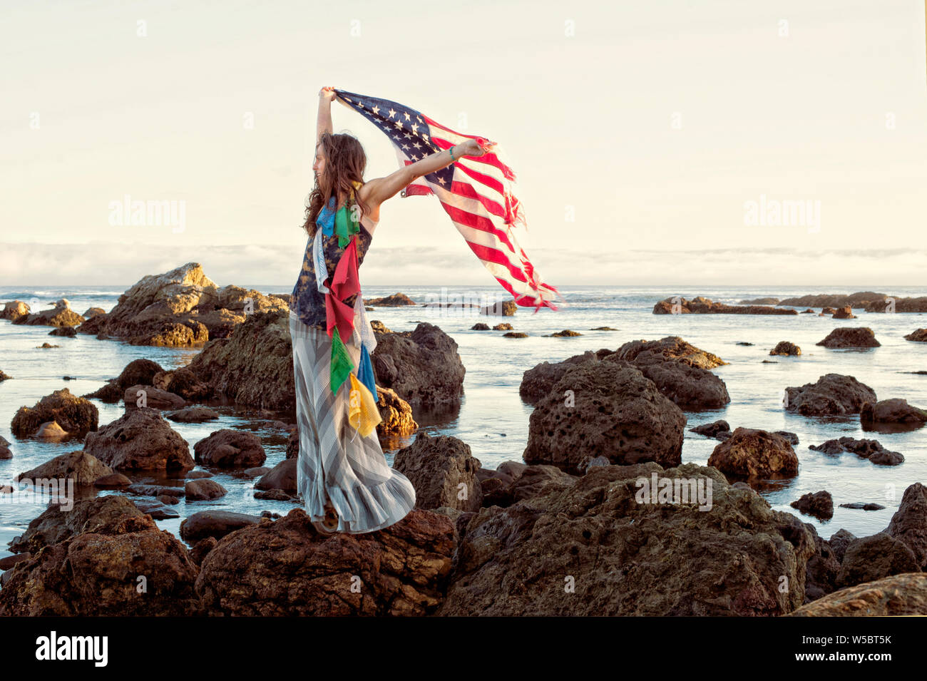 Femme par la mer tenue drapeau américain et portant une guirlande de prière tibétain flages. Banque D'Images Femme par la mer tenue drapeau américain et portant une guirlande de prière tibétain flages. Banque D'Images
