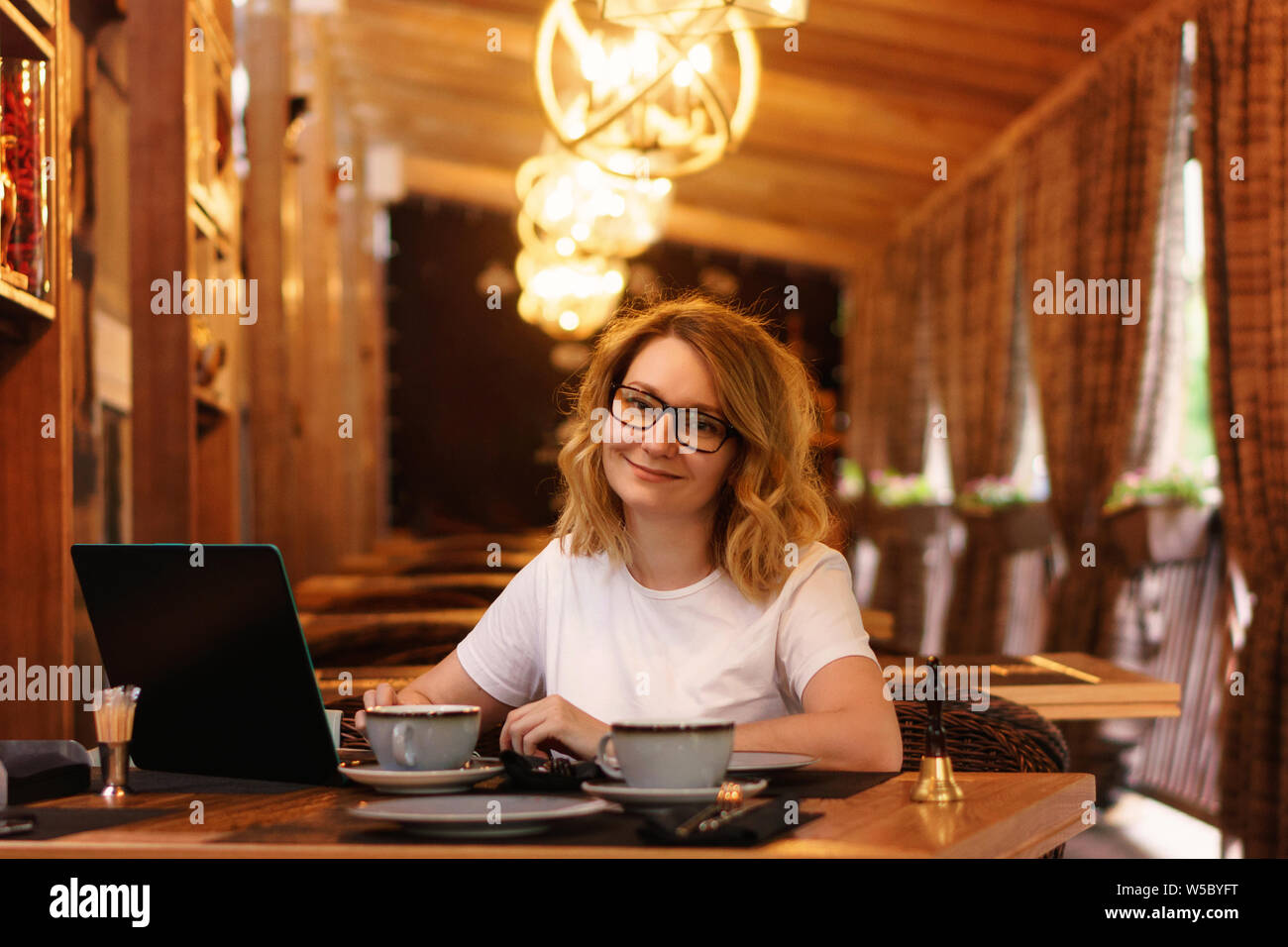 Dame d'affaires smiling at camera. Fille travaille à un ordinateur portable dans l'attente d'une commande sur une terrasse d'été du restaurant. Déjeuner d'affaires Banque D'Images