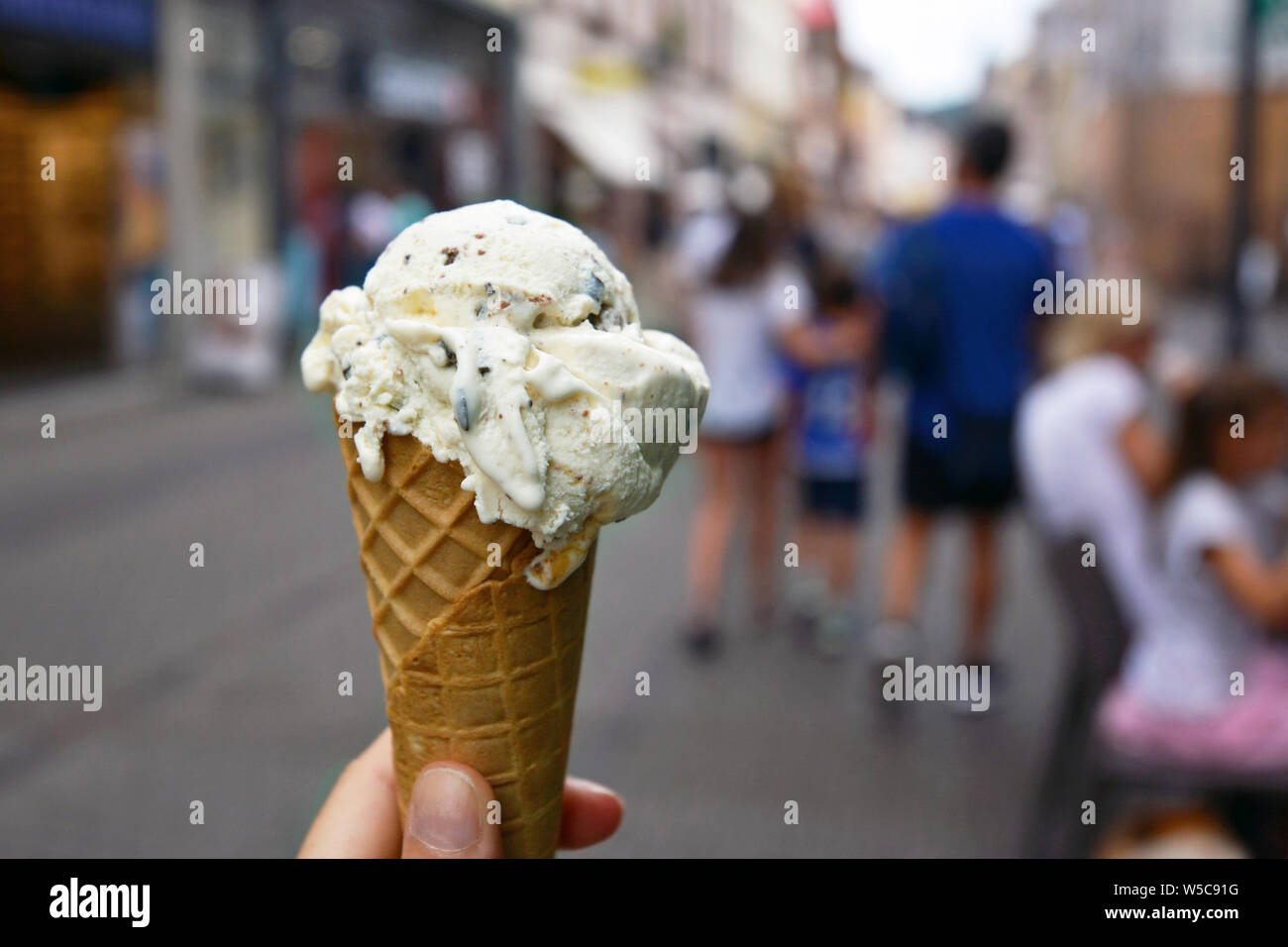 Close up of hand holding cône avec la vanille avec morceaux de chocolat avec de la crème glacée de la ville floues en arrière-plan de scène Banque D'Images