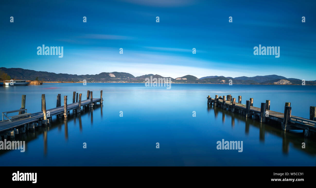 Deux jetée en bois ou jetée sur un lac bleu coucher du soleil et ciel nuageux la réflexion sur l'eau. L'exposition longue lac Massaciuccoli, Versilia, Toscane, Italie. Banque D'Images