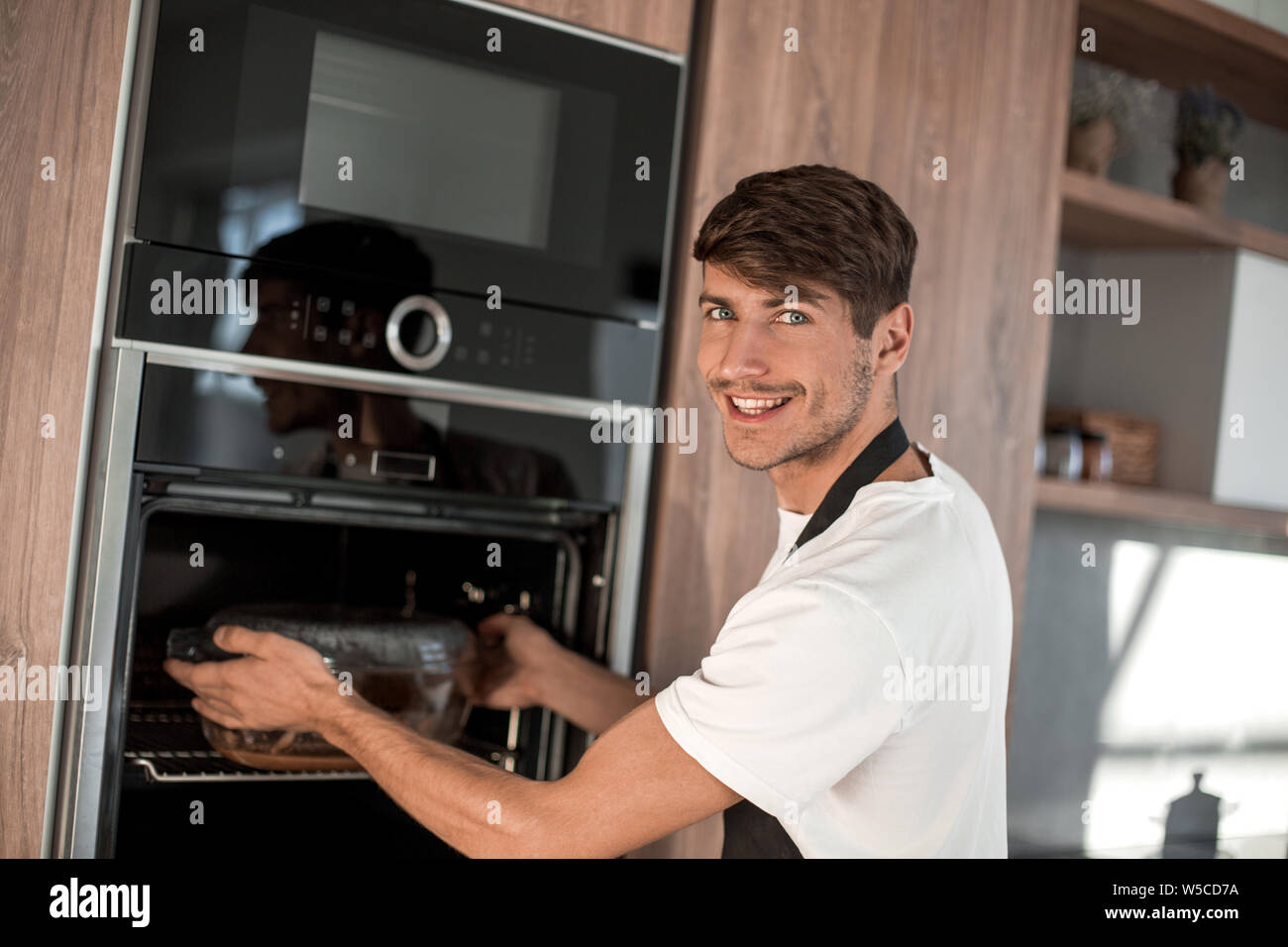 Smiling young man réchauffe le dîner dans sa cuisine Banque D'Images