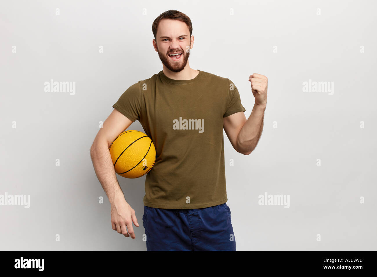 Les jeunes heureux et excité man holding basket ball sur fond isolé . guy célébrant la victoire et élever les mains, le ventilateur est de se réjouir de son succès Banque D'Images