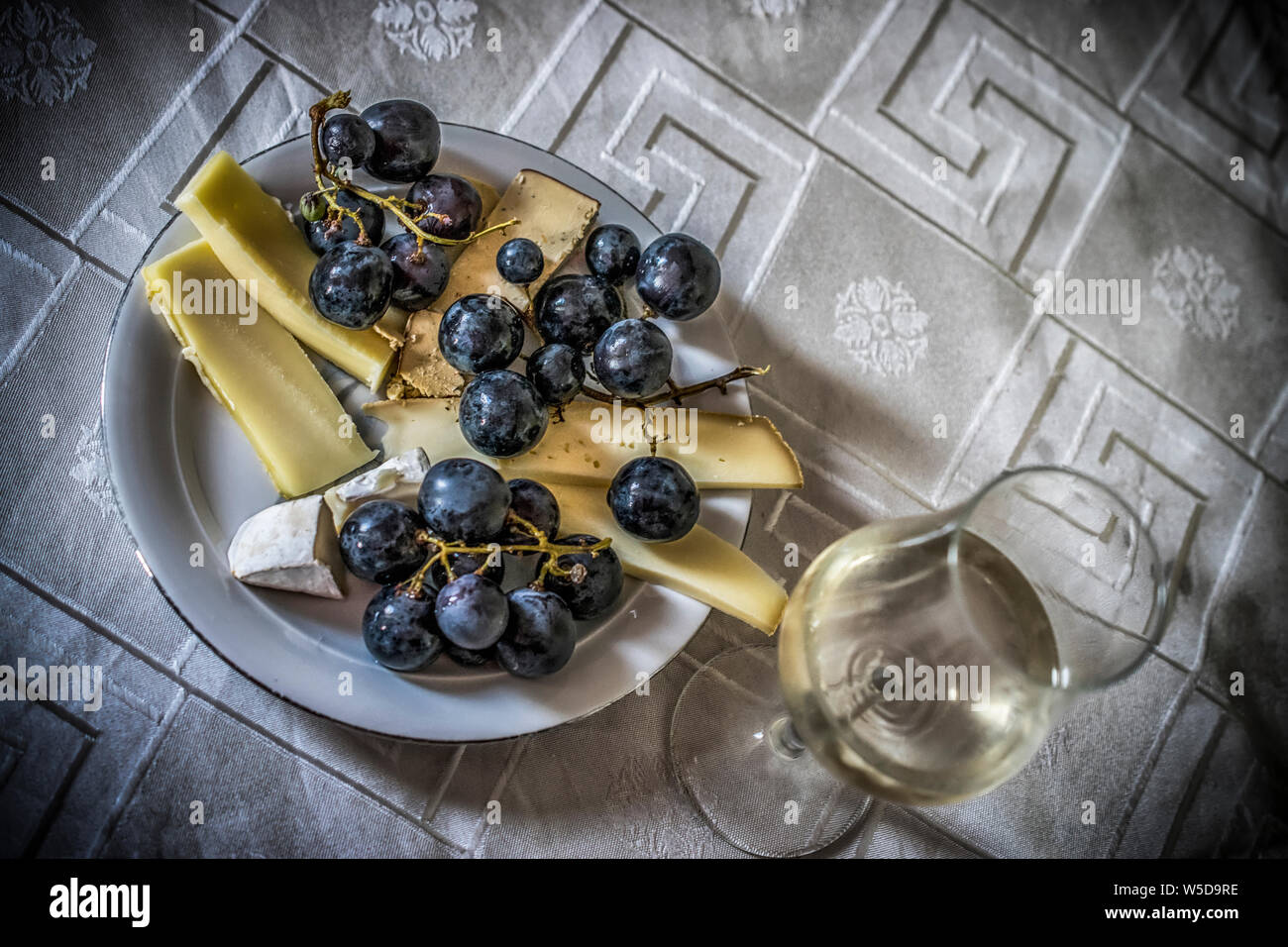 Une nature morte avec du fromage français, le raisin noir et un verre de vin blanc Banque D'Images