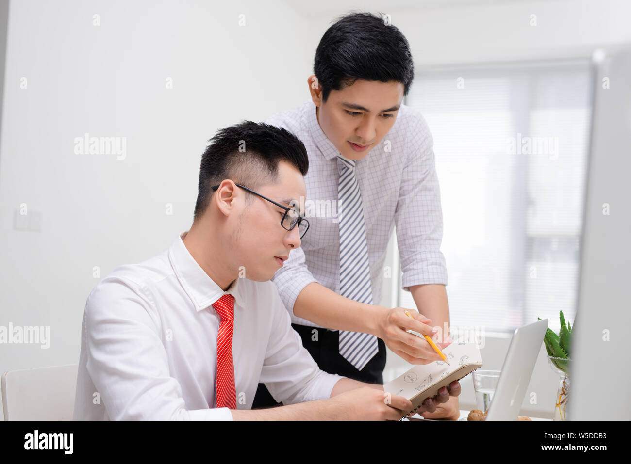 Deux hommes d'affaires travaillent ensemble avec l'ordinateur de bureau à bureau, l'un d'eux faisant à l'écran. Banque D'Images