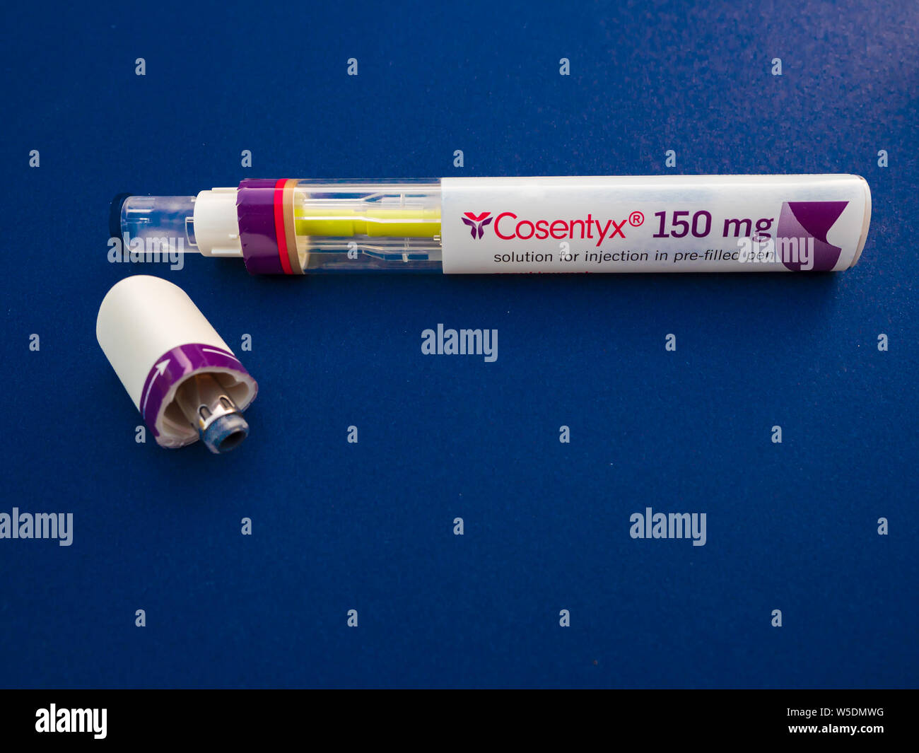 Un Cosentyx secukinumab (utilisé) 150mg injection automatique montrant l'utilisation de plumes jaune Indicateur de marque et le couvercle sur le côté sur un fond bleu Banque D'Images