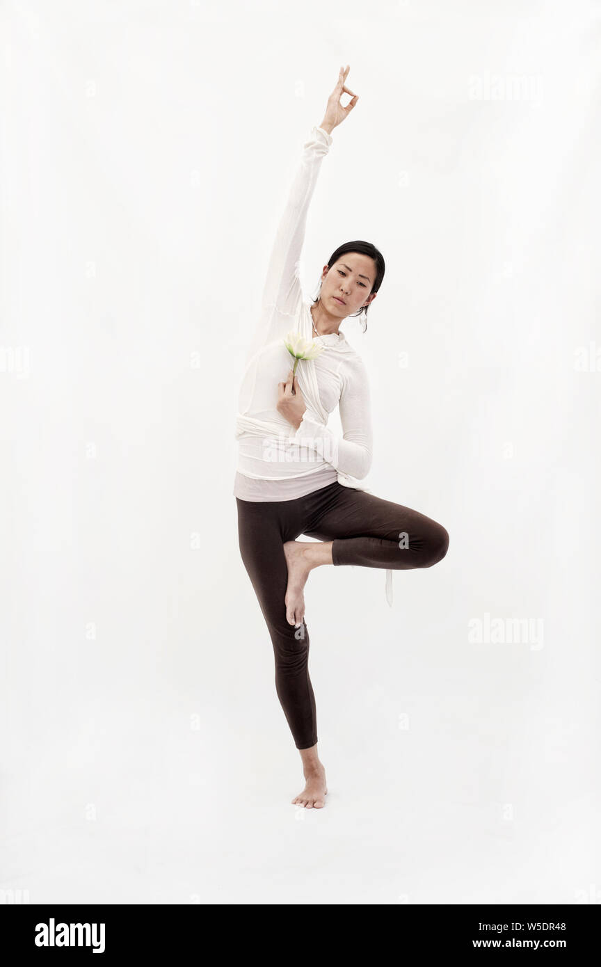 Belle asiatique spirituel Korean American Woman holding une fleur de lotus et d'équilibre dans une version du Yoga posture de l'arbre. Banque D'Images