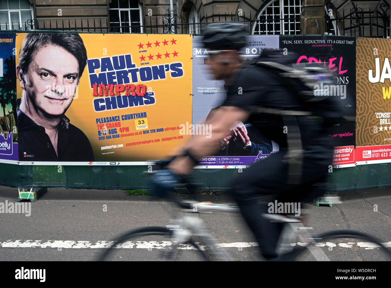 Un cycliste rides par des affiches publicitaires pour Paul Merton Chums Impro show sur à l'Edinbugh Fringe Festival. (With motion blur) Banque D'Images