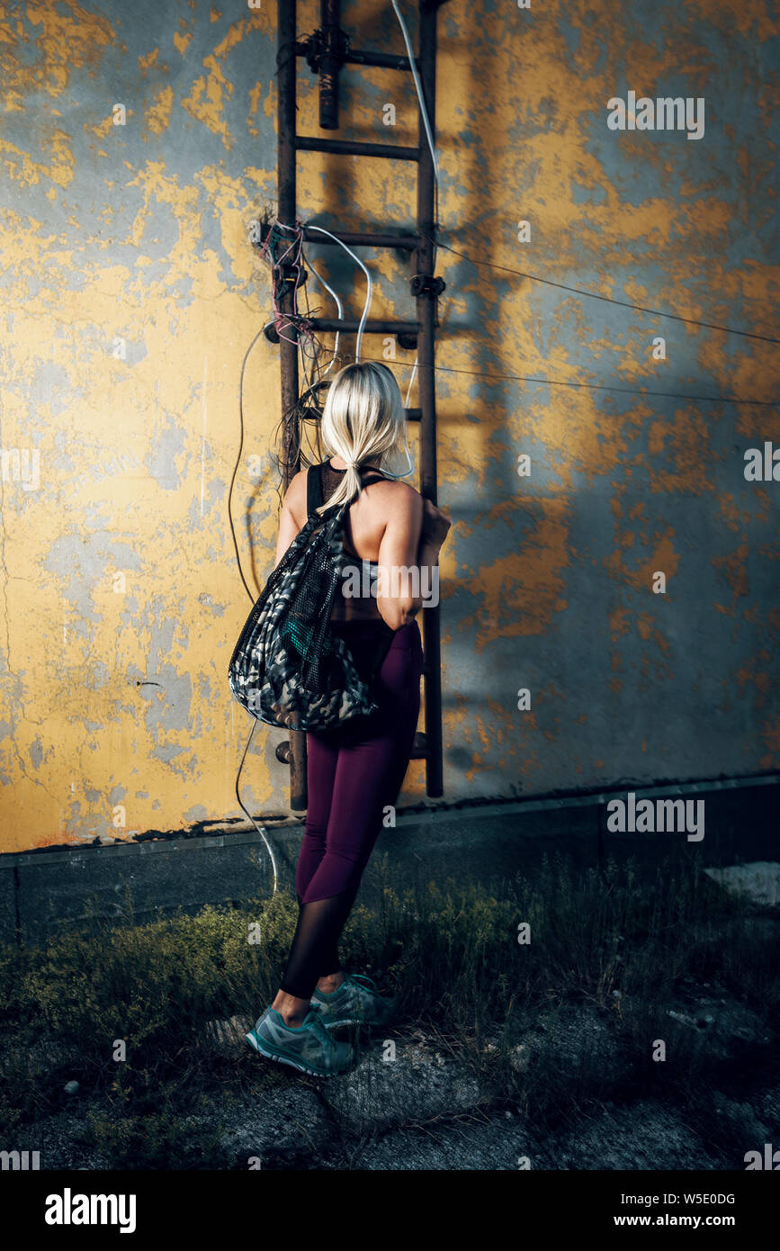 Jolie femme blonde avec de l'équipement de conditionnement physique et le sac debout sur le toit du bâtiment. La tonalité de l'image. Banque D'Images