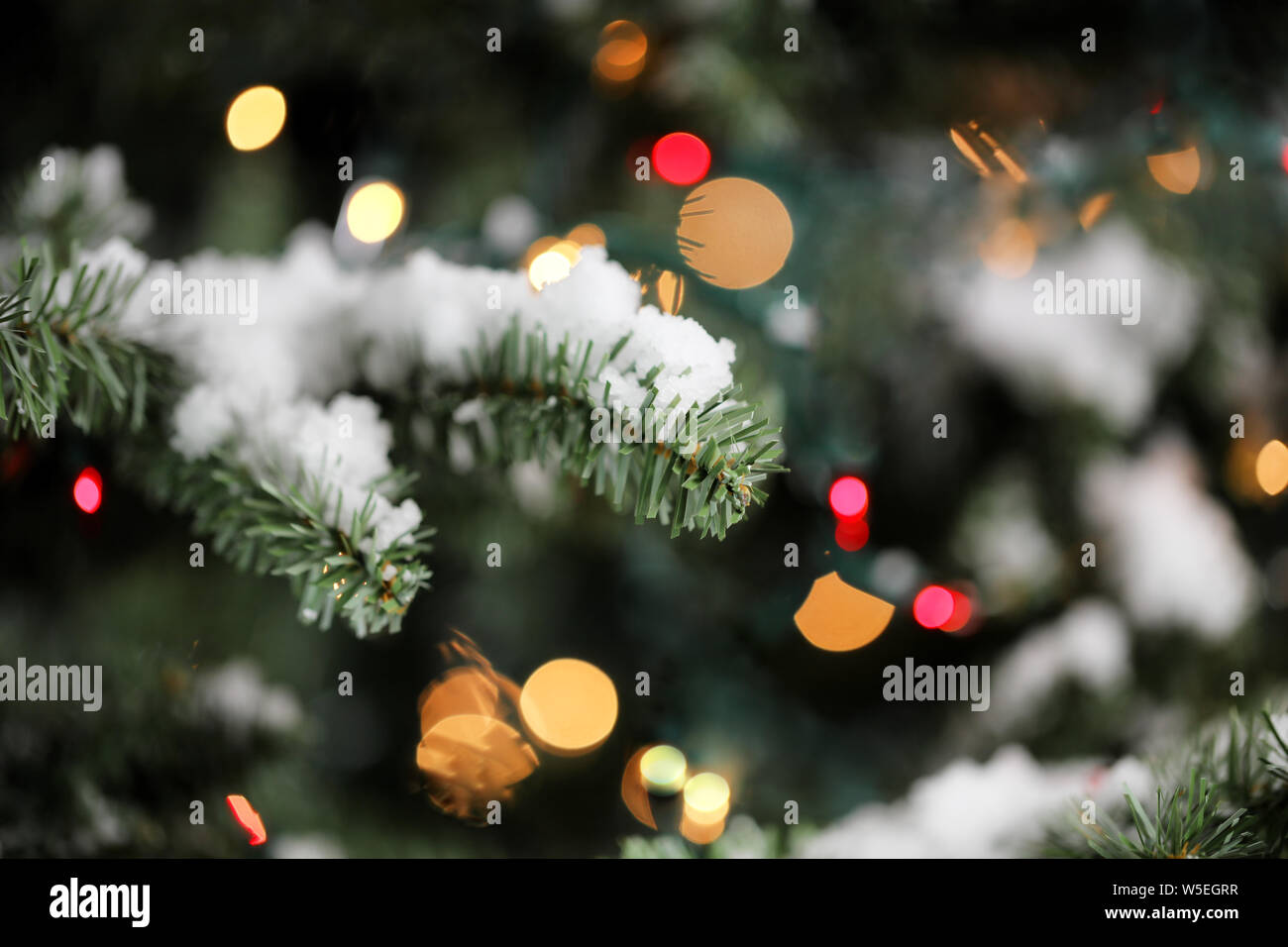 Arbre de Noël artificiel traditionnel avec des lumières brillantes et neige en arrière-plan Banque D'Images
