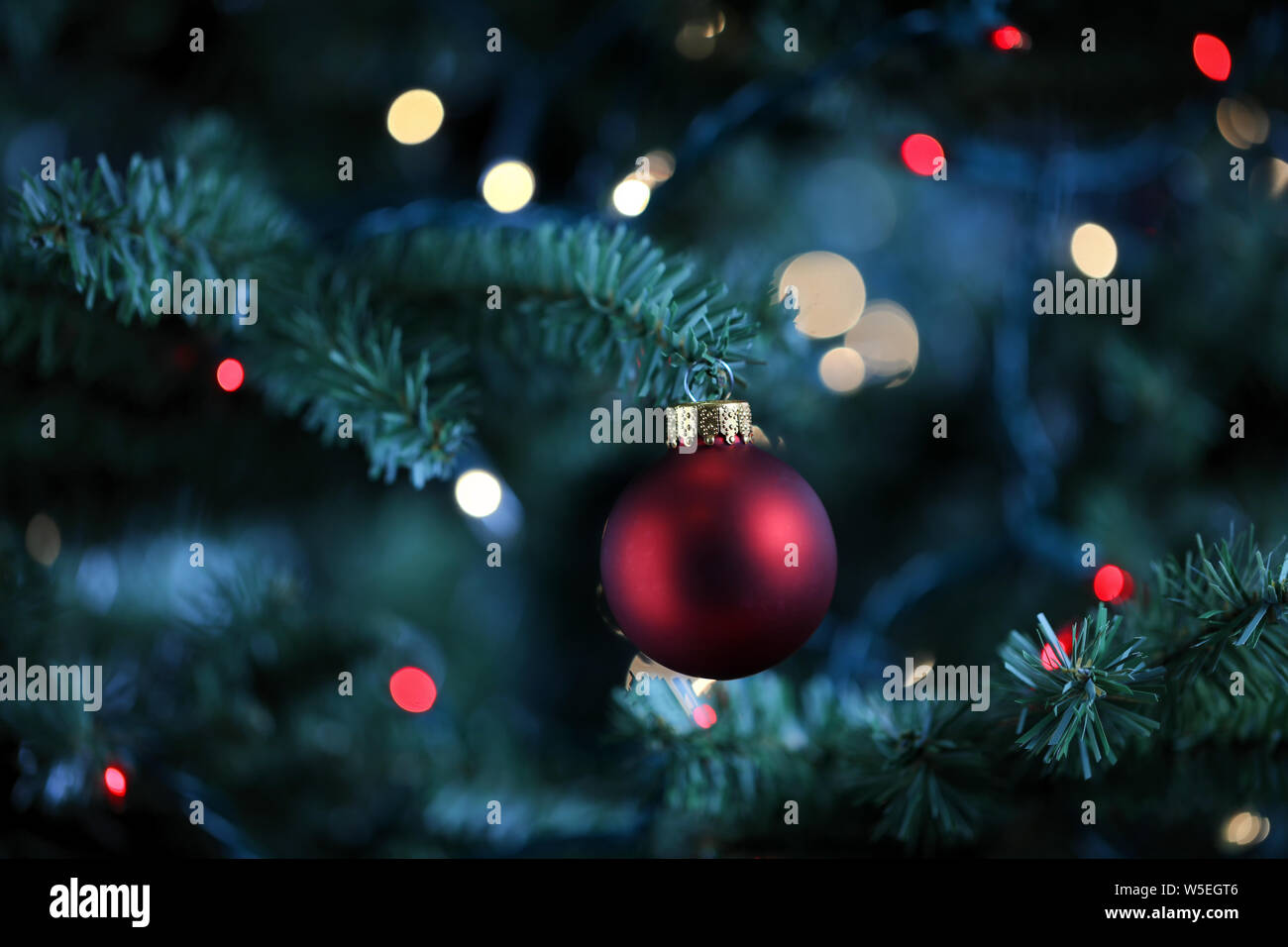 Arbre de Noël artificiel traditionnel avec une boule rouge ornement et incandescent lumières colorées en arrière-plan Banque D'Images