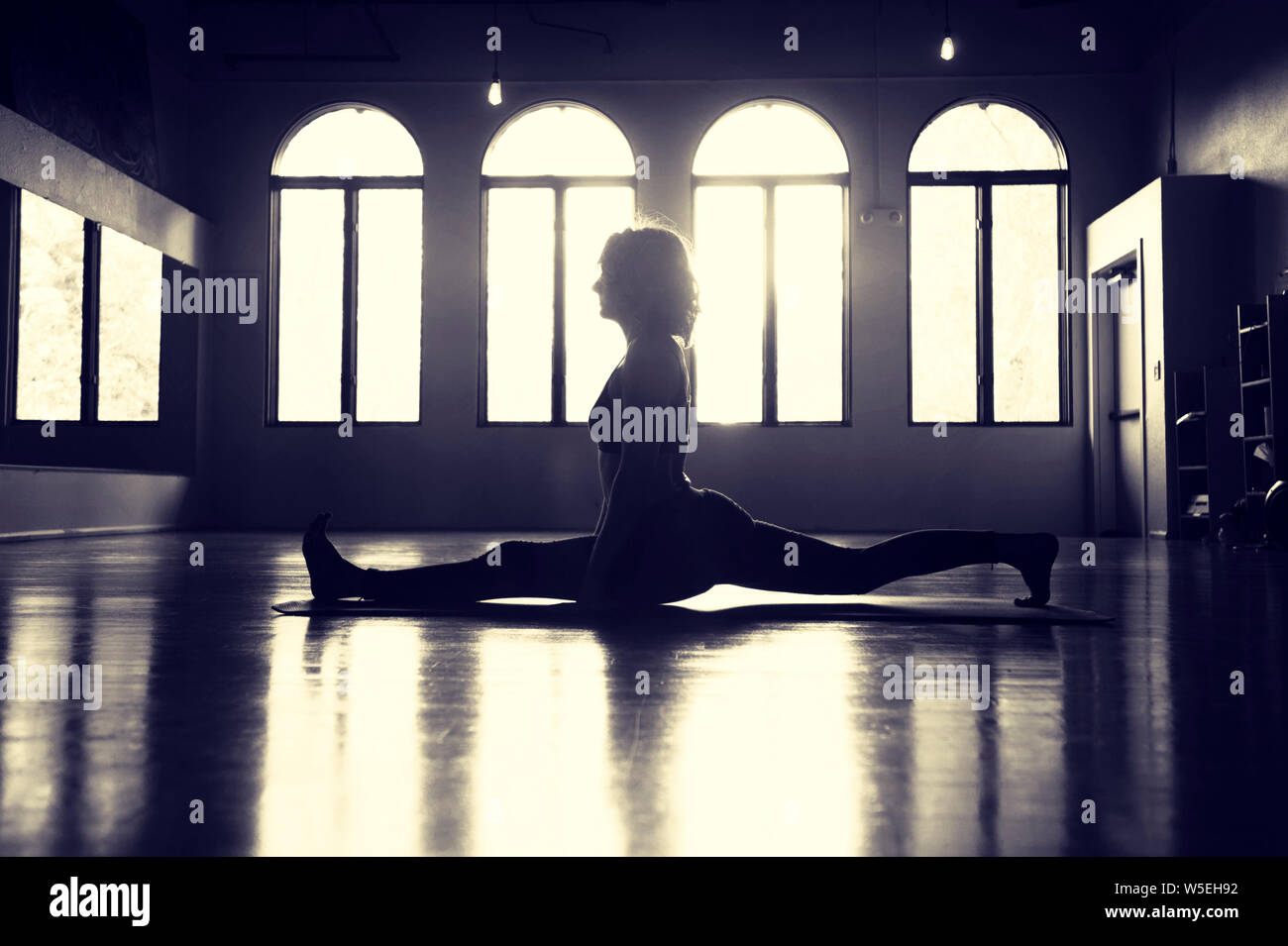 Moody silhouette d'une femme pratiquant le yoga se divise dans un ancien studio de ballet avec de belles fenêtres. Banque D'Images