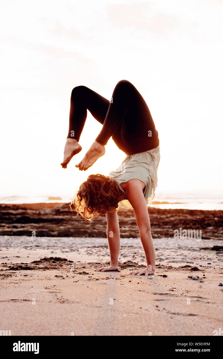 Mettre en place jeune femme sur la plage dans le Scorpion ou Vrksasans yoga posture. Banque D'Images