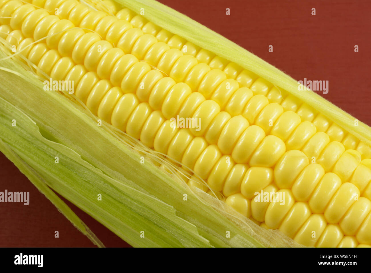 Close up de matières premières fraîches sur le maïs jaune s/n avec des feuilles et des plantes soie sur fond rouge Banque D'Images