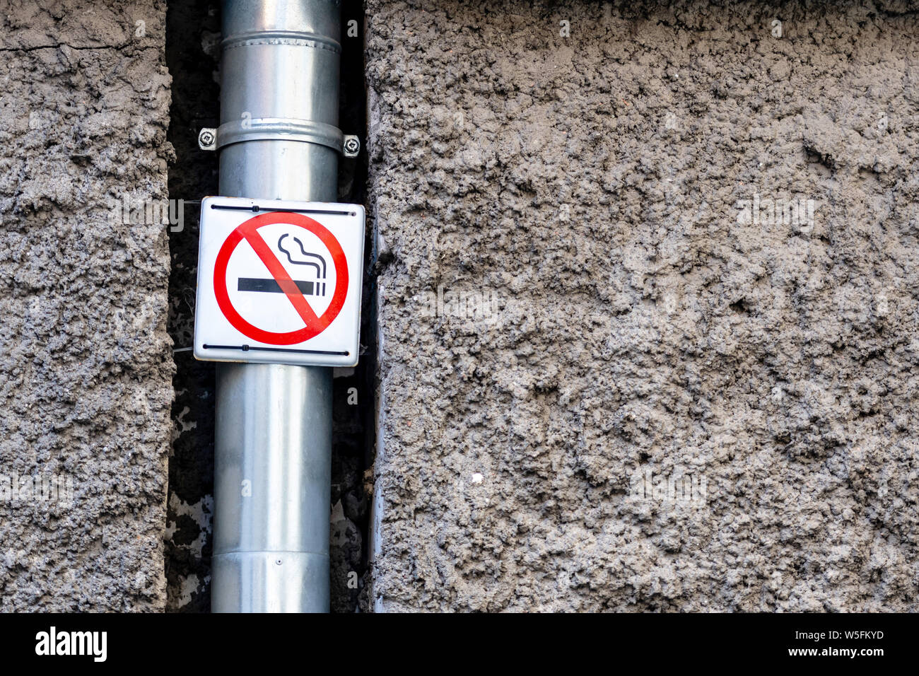 Mur extérieur décoratif plâtre avec surface en relief. Metal gutter. Panneau interdisant l'usage du tabac. - Image Banque D'Images
