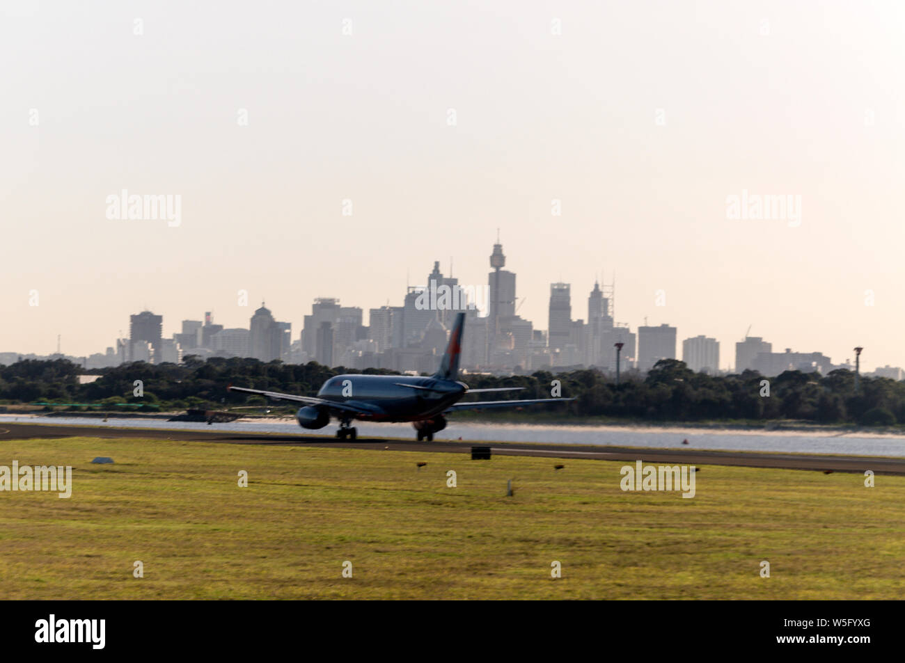 Un Jetstar prend le décollage sur la piste contre les gratte-ciel du centre-ville de Sydney à l'aéroport de Sydney (Kingsford Smith) près de Sydney en Nouvelle-Galles du Sud, en Australie Banque D'Images