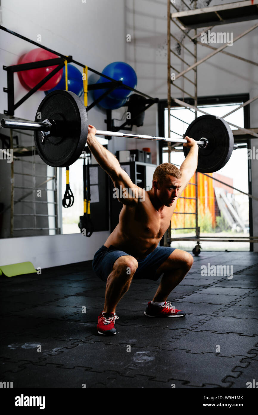 L'homme musclé faisant squats avec barbell in a gym Banque D'Images