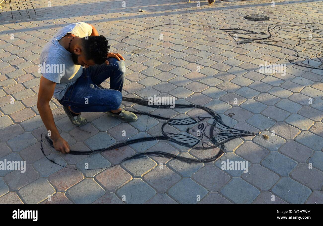 (190729) -- Gaza, 29 juillet 2019 (Xinhua) -- colporteur palestinienne Maawiya Ashour peint avec du charbon sur le sol comme un moyen d'amener les clients à acheter d'un plateau/bouilloire de son échoppe dans la ville de Gaza, le 28 juillet 2019. (Str/AFP) Banque D'Images