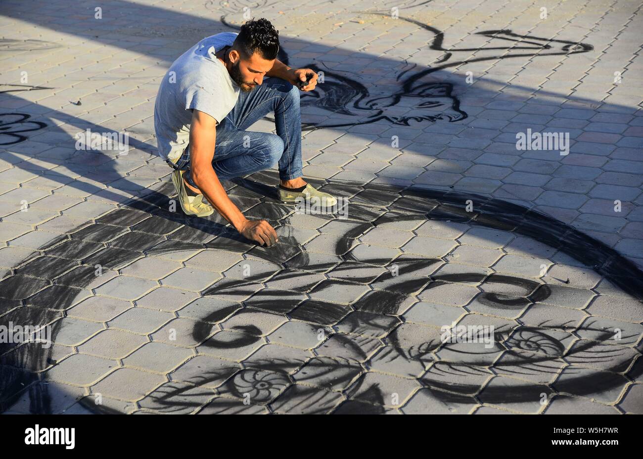 (190729) -- Gaza, 29 juillet 2019 (Xinhua) -- colporteur palestinienne Maawiya Ashour peint avec du charbon sur le sol comme un moyen d'amener les clients à acheter d'un plateau/bouilloire de son échoppe dans la ville de Gaza, le 28 juillet 2019. (Str/AFP) Banque D'Images