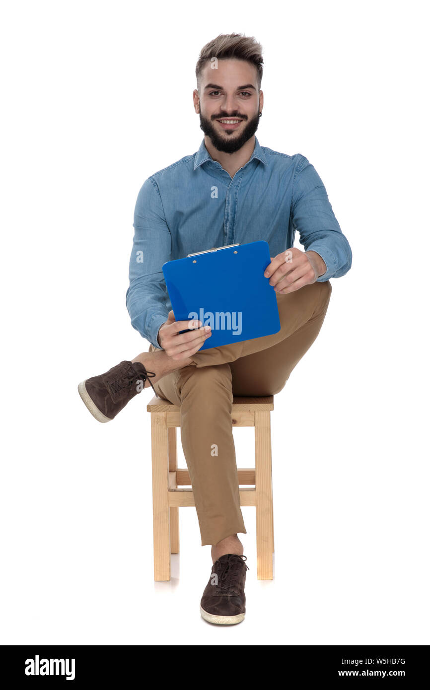 Homme assis avec un presse-papiers dans la main et les jambes croisées sur fond blanc Banque D'Images