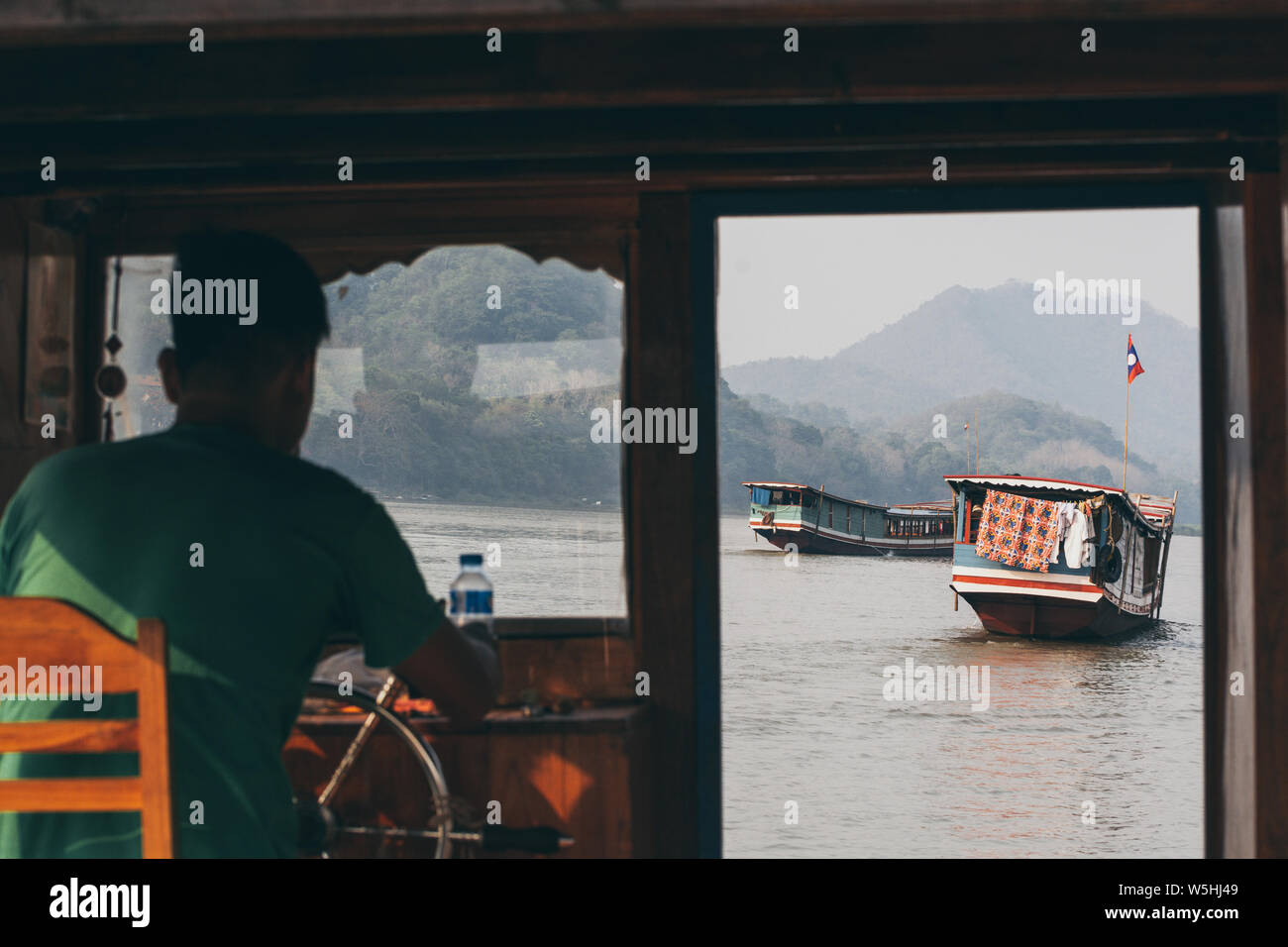 Luang Prabang, Laos - Mai 2019 : vue sur les bateaux traditionnels en bois laotien lent sur le fleuve du Mékong à travers la fenêtre du capitaine de pilotage. Banque D'Images