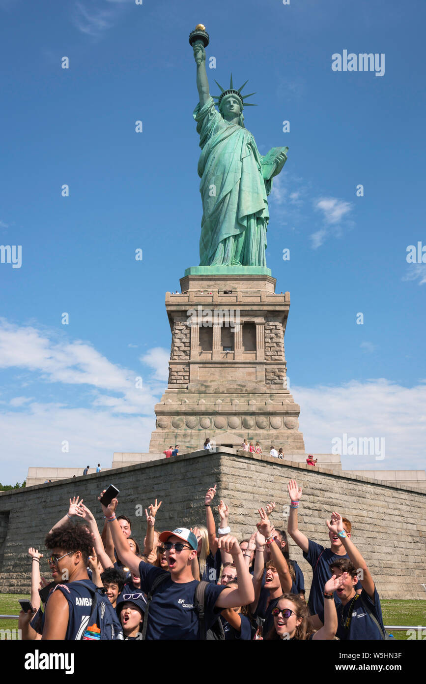 Tourisme à New York, vue d'un groupe de jeunes élèves en train d'encourager tout en étant photographié à la base de la Statue de la liberté, New York City, USA. Banque D'Images