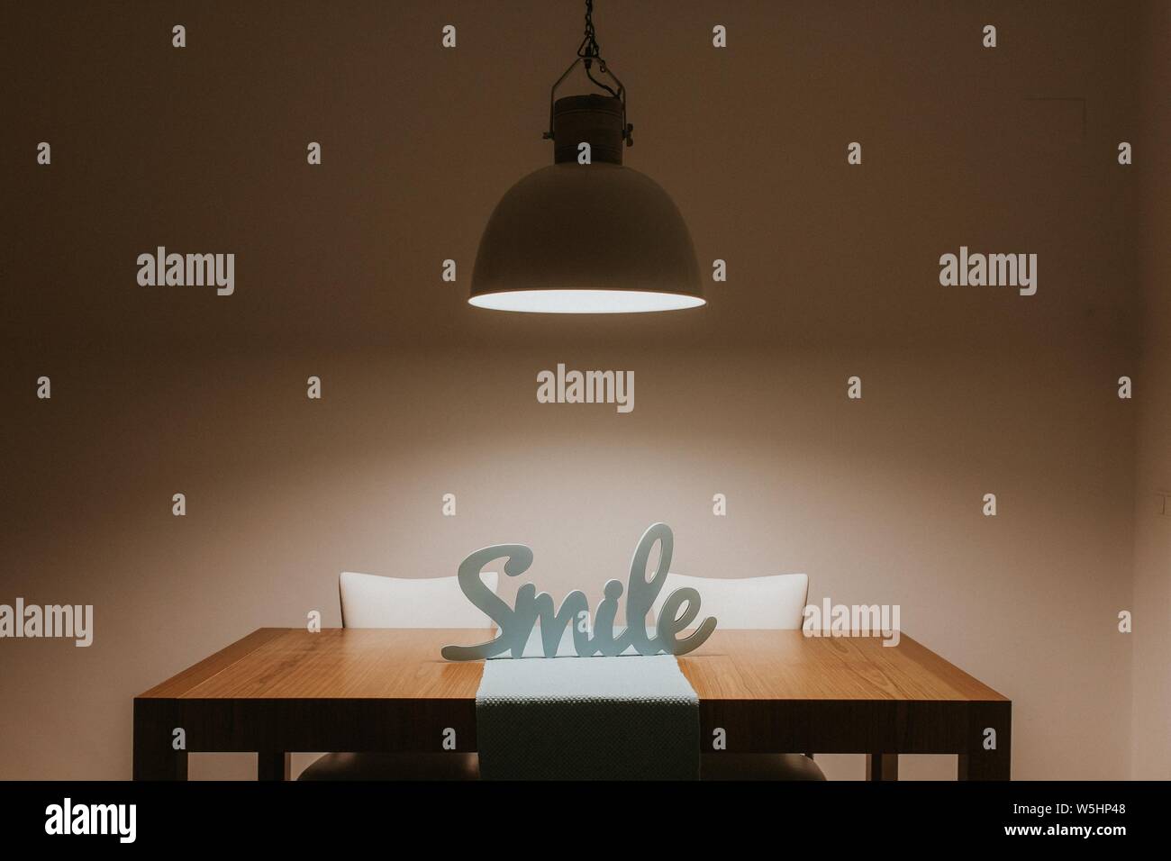 Photo d'un panneau blanc découpé « Smile » sur une table avec deux chaises blanches et une suspension au-dessus Banque D'Images
